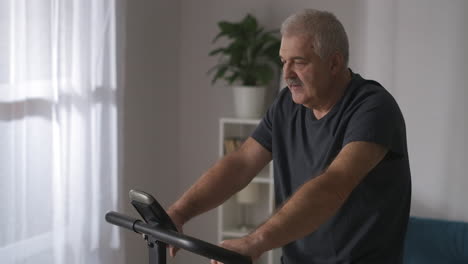 portrait-of-middle-aged-man-training-with-stationary-bike-at-home-caring-about-health-keeping-fit-in-old-age-sport-activity